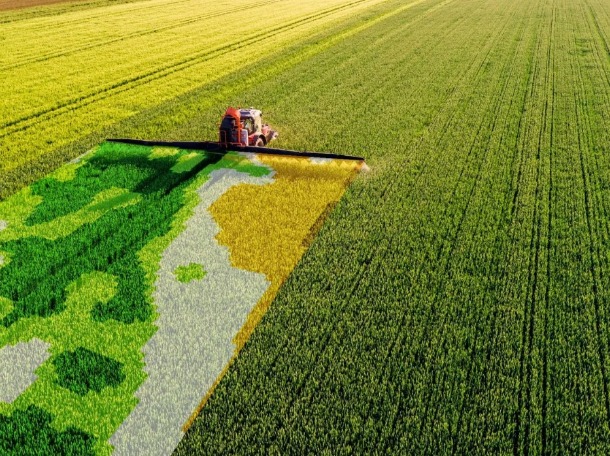 Aerial view of a tractor spraying a wheat field, with a satellite-style crop-health map overlaid on part of the field